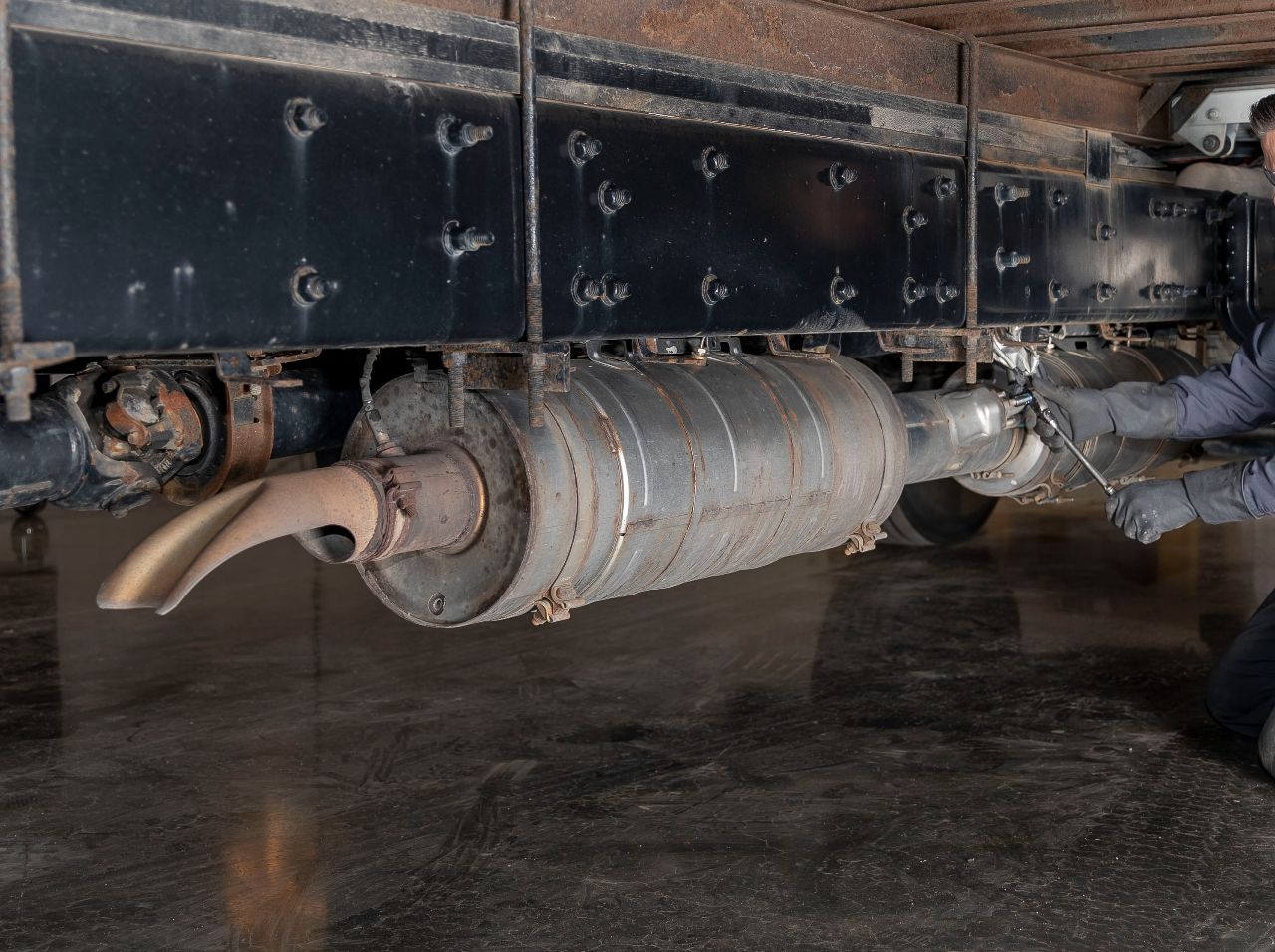 Technician servicing diesel truck exhaust system and DPF filter underneath heavy-duty vehicle chassis frame area