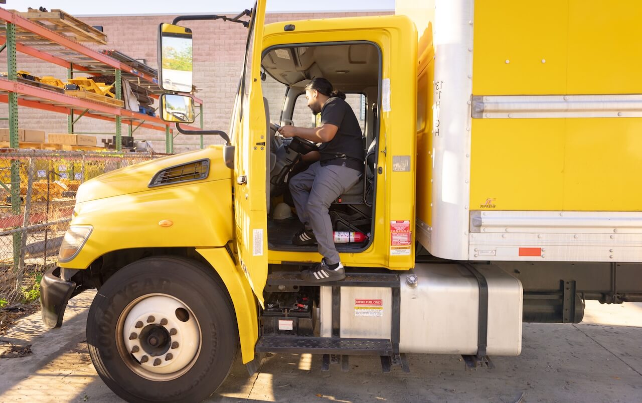 Mobile truck repair service vehicle with open rear compartment and liftgate as technician inspects equipment in outdoor lot beside trailers
